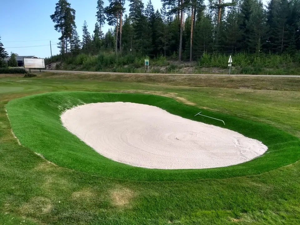 Valkoisella hiekalla täytetty bunkkeri, jonka reunat ovat tekonurmea.