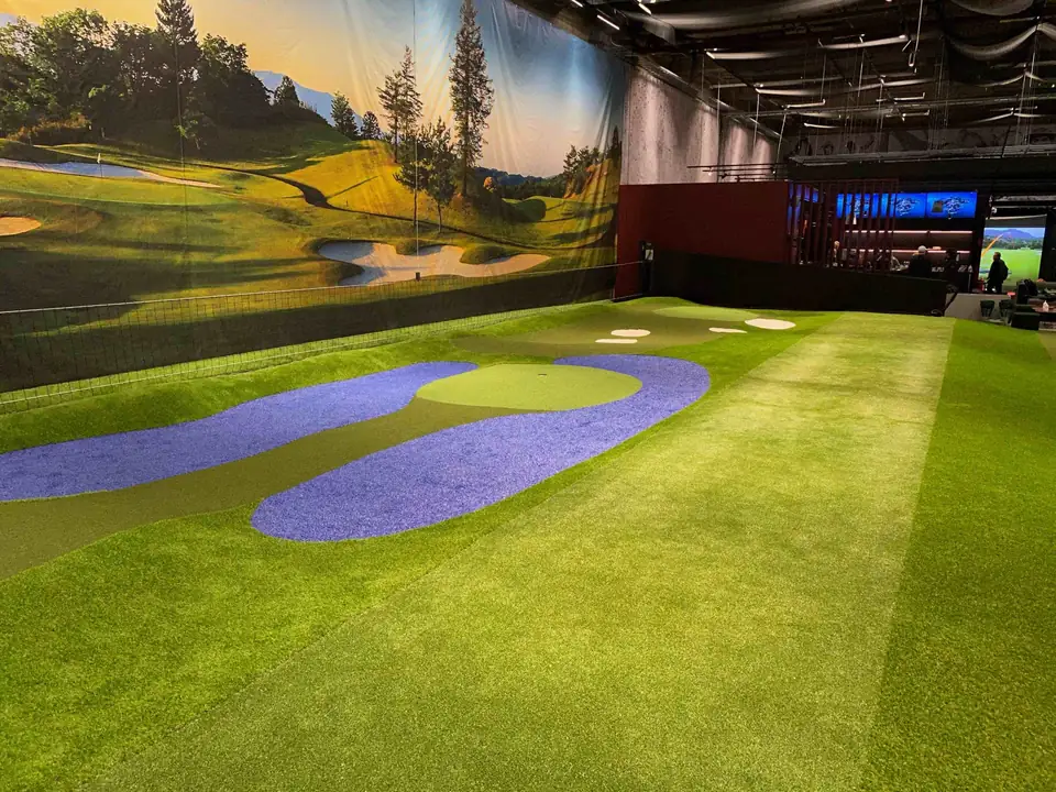 GoGolf Loungen halli: sininen vesinurmi ja viheriöt golfkenttämaalauksen edessä.