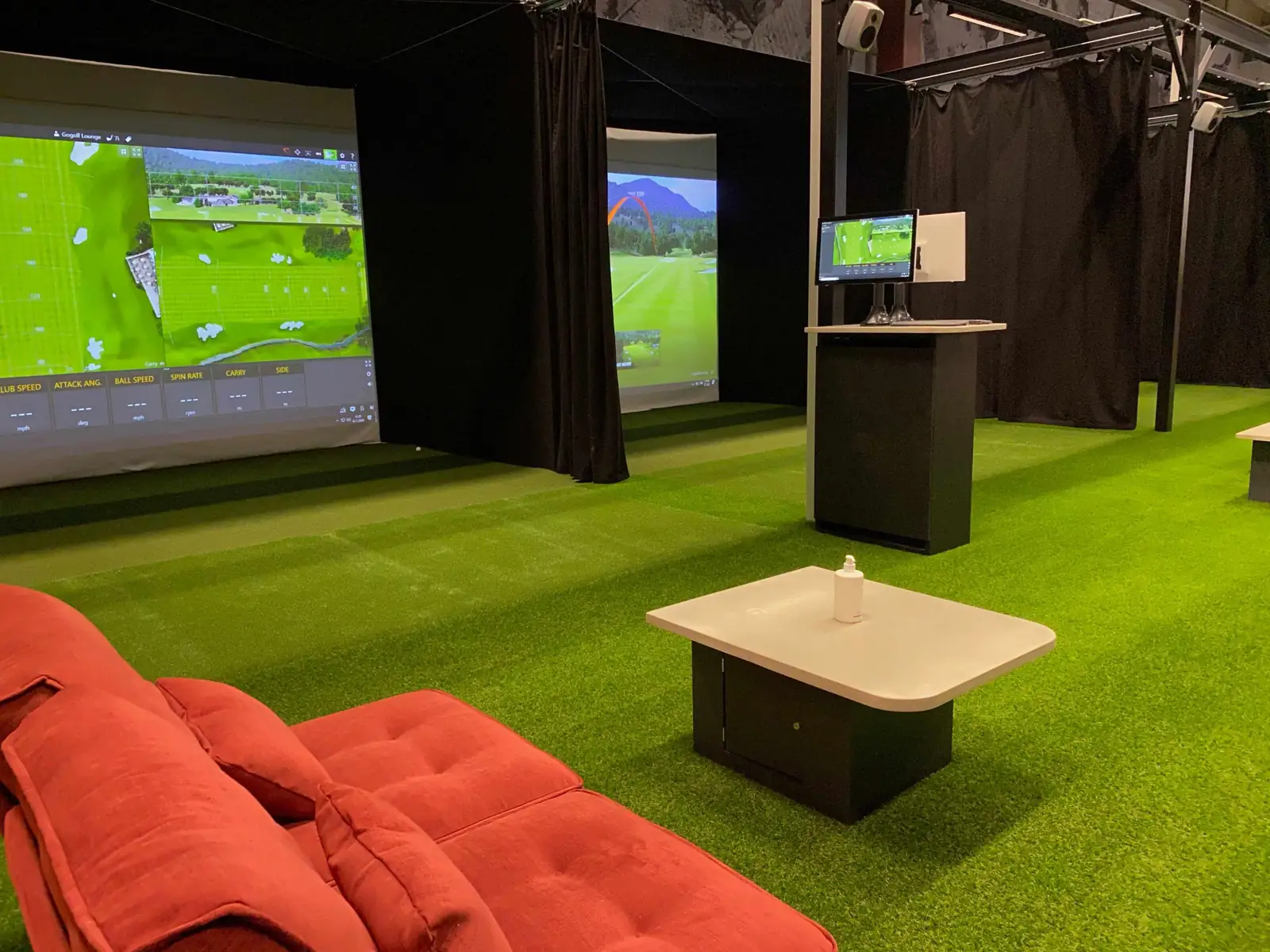 GoGolf Loungen simulaattoripaikka: valkokangas, vihreä tekonurmi, sohva ja pöytä.
