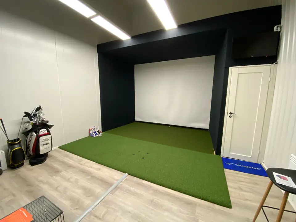 Golf Garage Vantaan simulaattori: musta kehys, valkokangas ja tekonurmi.