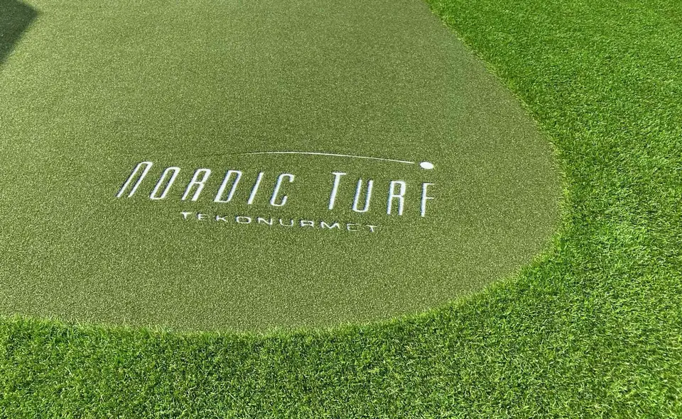 Nordic Turfin logo valkoisena kuviona tekonurmiviheriön pinnassa.