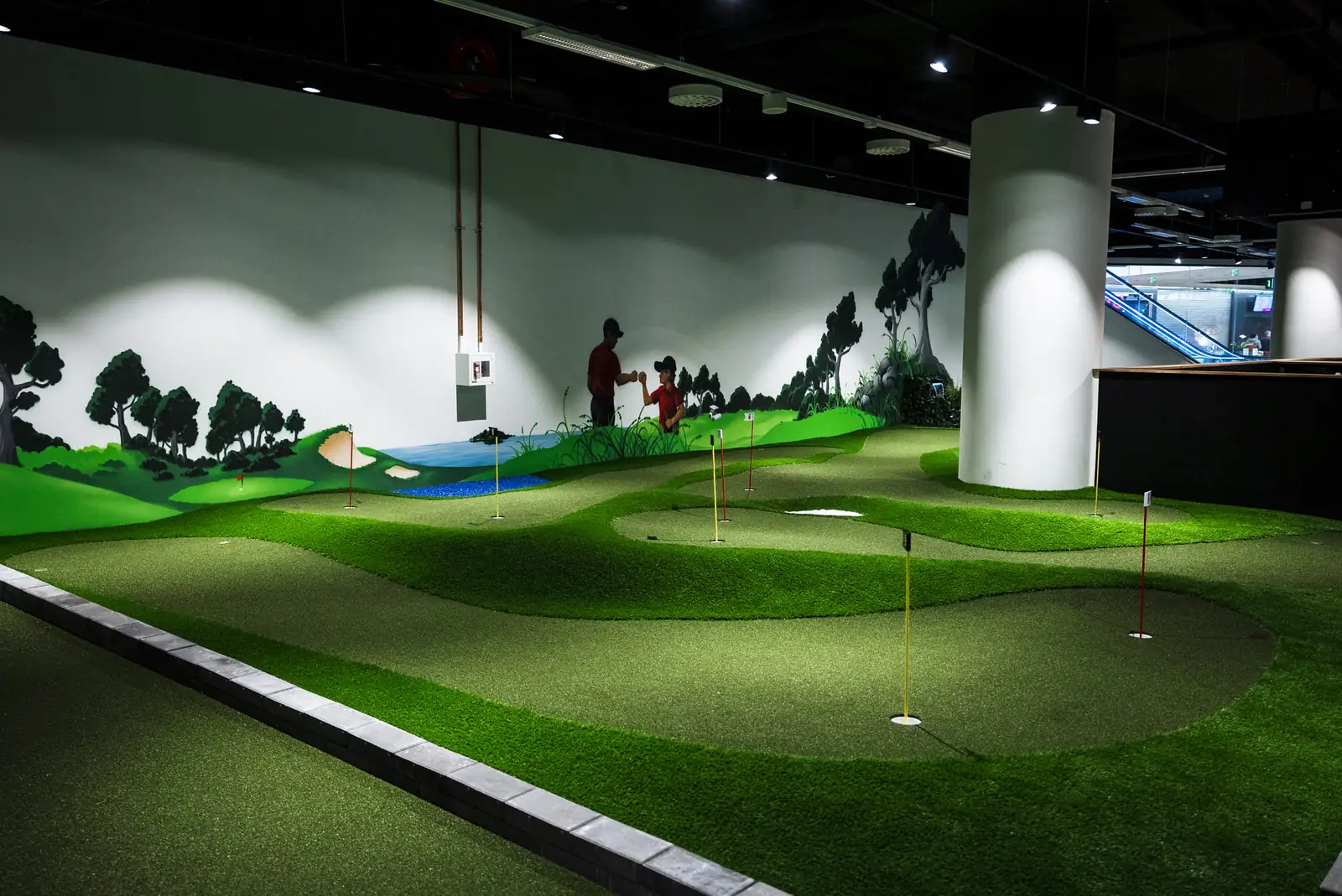 Bogey Parkin sisäminigolfrata: kumpuilevat viheriöt, liput ja golfmaisema seinämaalauksena.