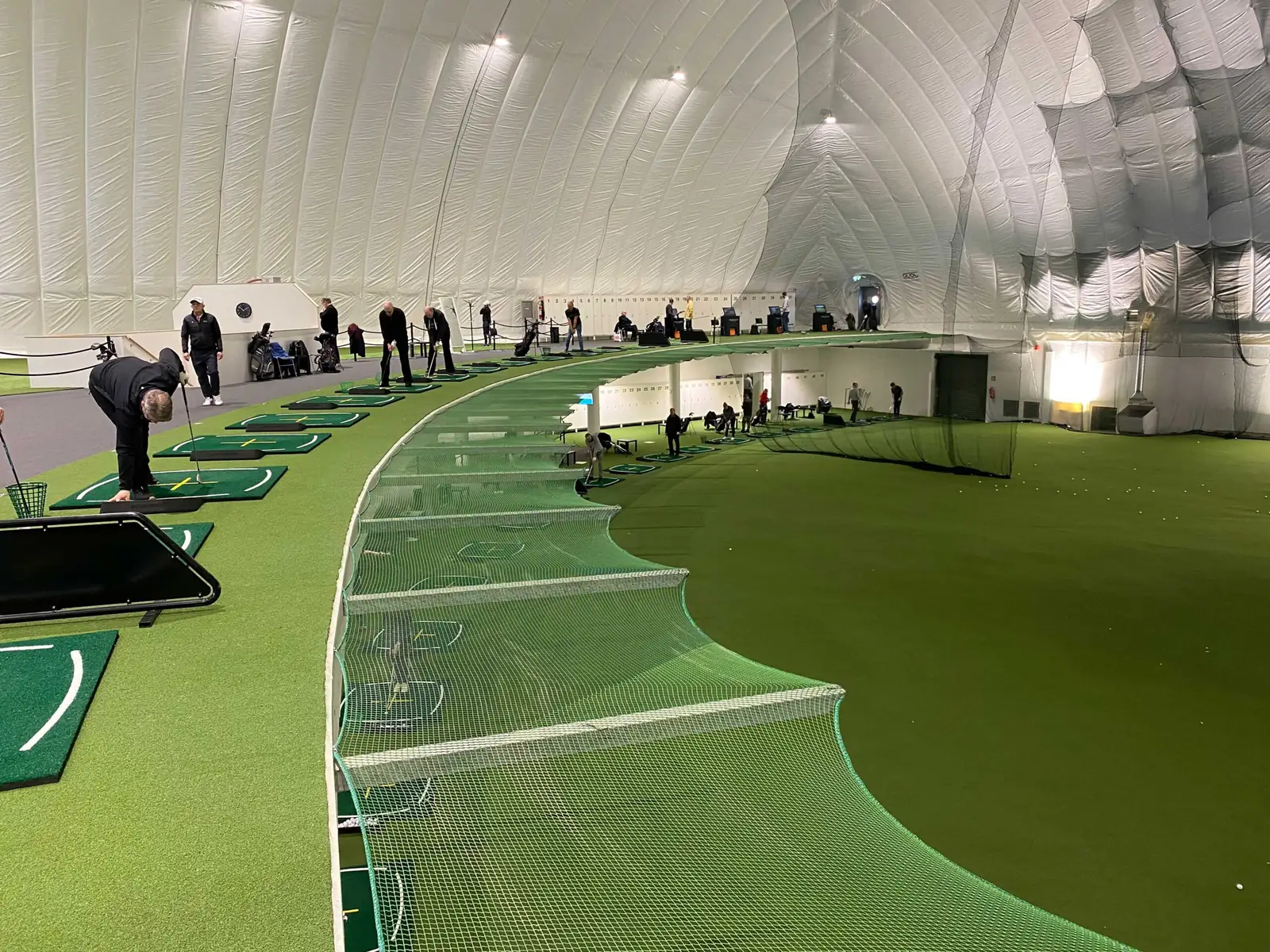 Season Golfin hallin yläkerta: kaareva rivi lyöntipaikkoja verkkojen takana ja niiden edessä viheriö.