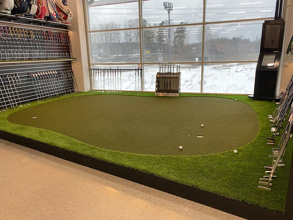 Viheriö reunanurmineen golfmyymälän lattialla suuren ikkunan edessä.