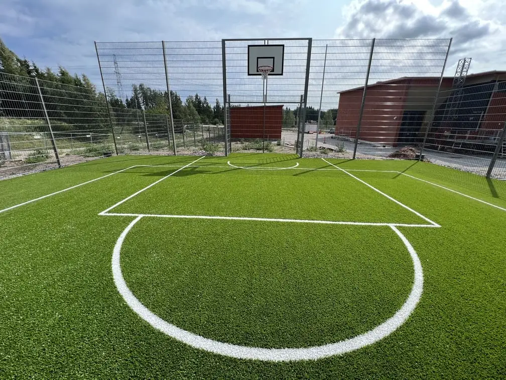 Saman kentän keskiympyrä ja rajaviivat läheltä, taustalla koripallokori ja aita.