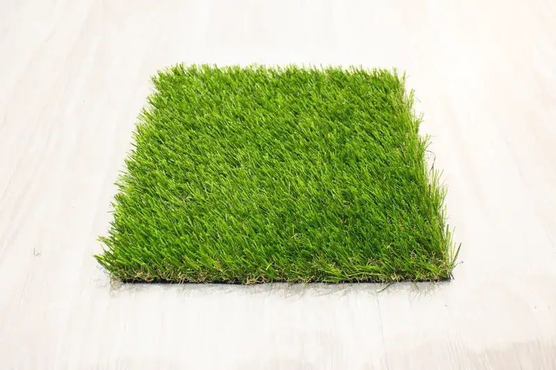 Noin 20 × 30 cm tekonurmen näytepala vaalealla lattialla.